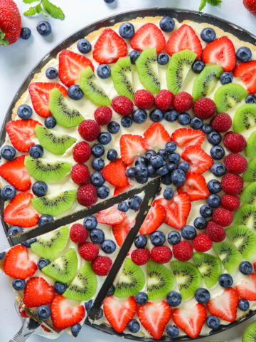 Pizza aux Fruits avec une part levée et des fraises et kiwis à proximité