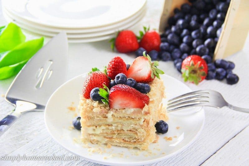 Easiest Napoleon cake recipe. Layered with delicious cream and garnished with fresh berries. #napoleoncake #russiannapoleon #napoleon #layeredcake #puffpastrycake Slice of Simple Napoleon Cake with a fork and berries.