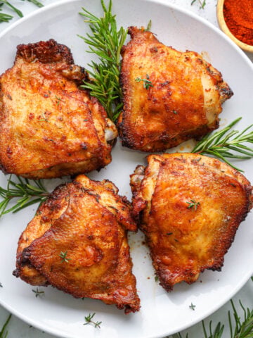 Horizontal image of Air Fryer Chicken Thighs on a white plate with rosemary sprigs.