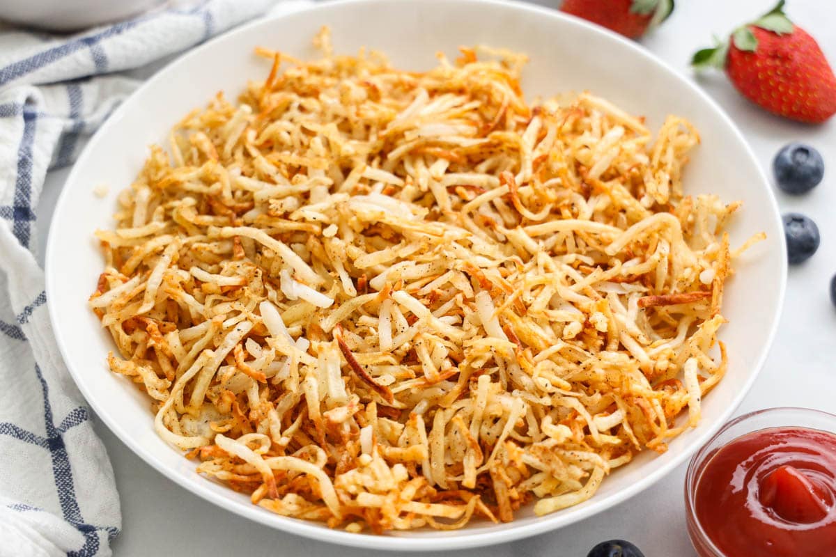 Crispy Air Fryer Hash Browns on a dish with ketchup and berries nearby.