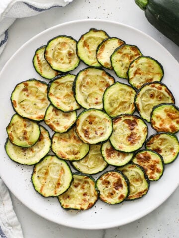 Air Fryer Zucchini layered on a white plate with a zucchini nearby