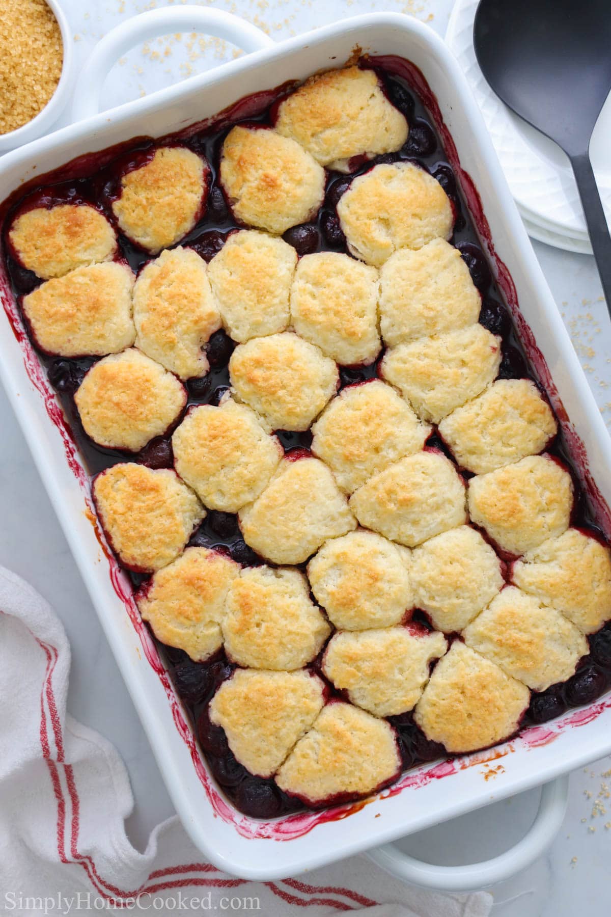 Cobbler aux cerises dans un plat de cuisson avec une cuillère et des assiettes à proximité