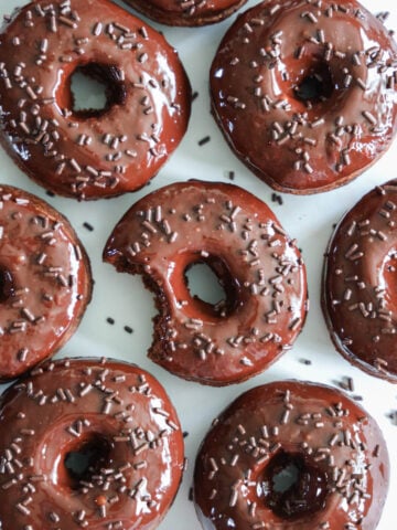 Chocolate Donuts covered in sprinkles, one with a missing bite