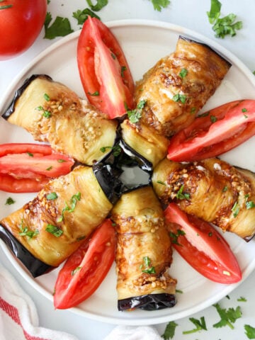 Image verticale d'Apéritifs d'aubergine assemblés sur une assiette blanche avec des quartiers de tomate
