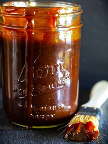 Vertical image of Homemade Barbecue Sauce in a mason jar with a brush nearby