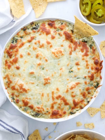 Bol de Trempette Chaude aux Artichauts avec chips et jalapenos à proximité.