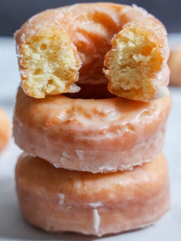 Vertical image of Old Fashioned Sour Cream Donuts in a stack with the top one missing a bite.