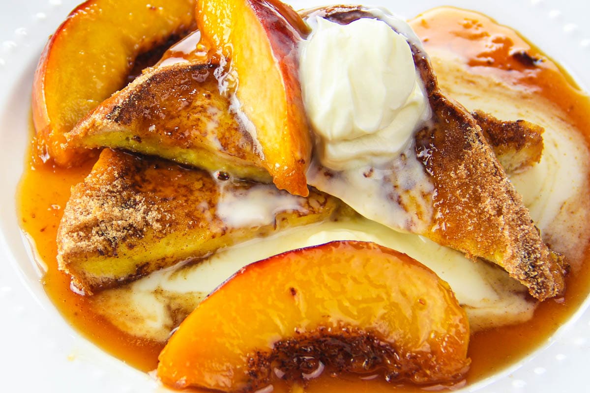 Cinnamon Peach French toast drizzled with caramelized rum and peach syrup. This easy recipe is topped with creme fraiche for the ultimate breakfast. #peachfrenchtoast #frenchtoast #peachsyrup #peachtaost #peachesandcream Gourmet Peach French Toast with peach syrup and garnished with creme fraiche.