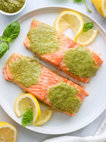 Pesto Salmon filets on a white plate with basil and lemon slices
