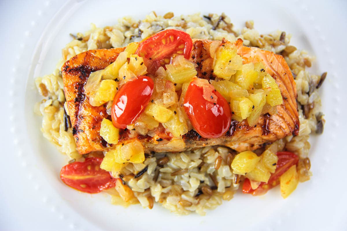 Quick grilled salmon recipe with sautéed onion, pineapple, and cherry tomatoes. Its the perfect summer salmon dish that is paleo and whole 30 approved. #ananasalmon #salmon #grilledsalmon #summerdinner #summersalmon Ananas Salmon covered with pineapple and cherry tomatoes on a bed of wild rice.