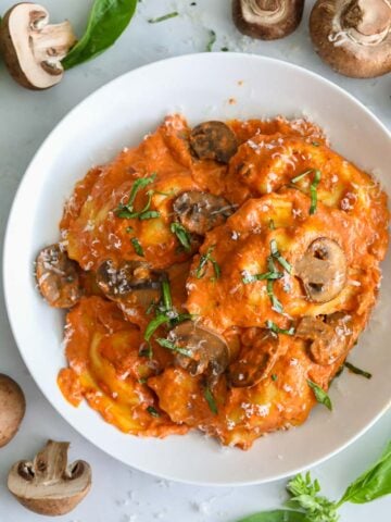 image aérienne de ravioli à la saucisse dans une assiette blanche avec des champignons et du basilic à côté