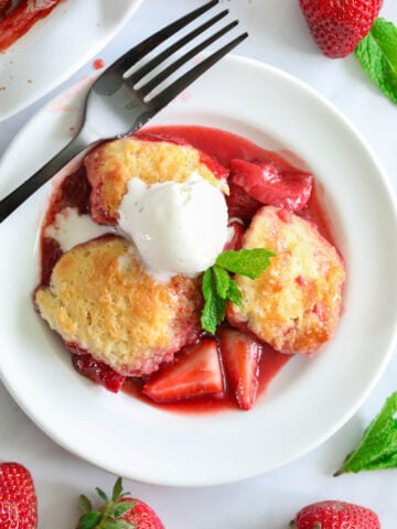 Cobbler aux fraises avec de la glace dans une assiette blanche avec une fourchette et des fraises à proximité