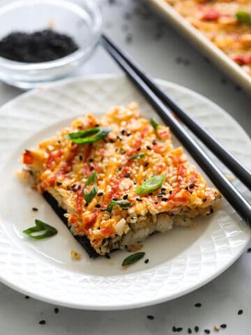 Easy Sushi Bake on a white plate with chopsticks, and a bowl of crumbled nori in the background.