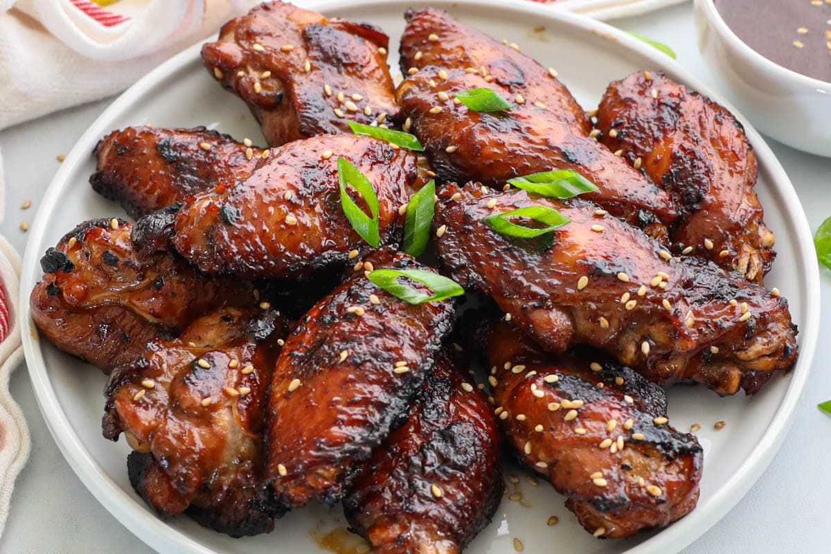 Assiette d'ailes de poulet teriyaki garnies d'oignon vert et de graines de sésame.