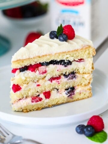 Tranche de gâteau chantilly aux baies sur le dessus sur une assiette blanche avec un support à gâteau bleu derrière