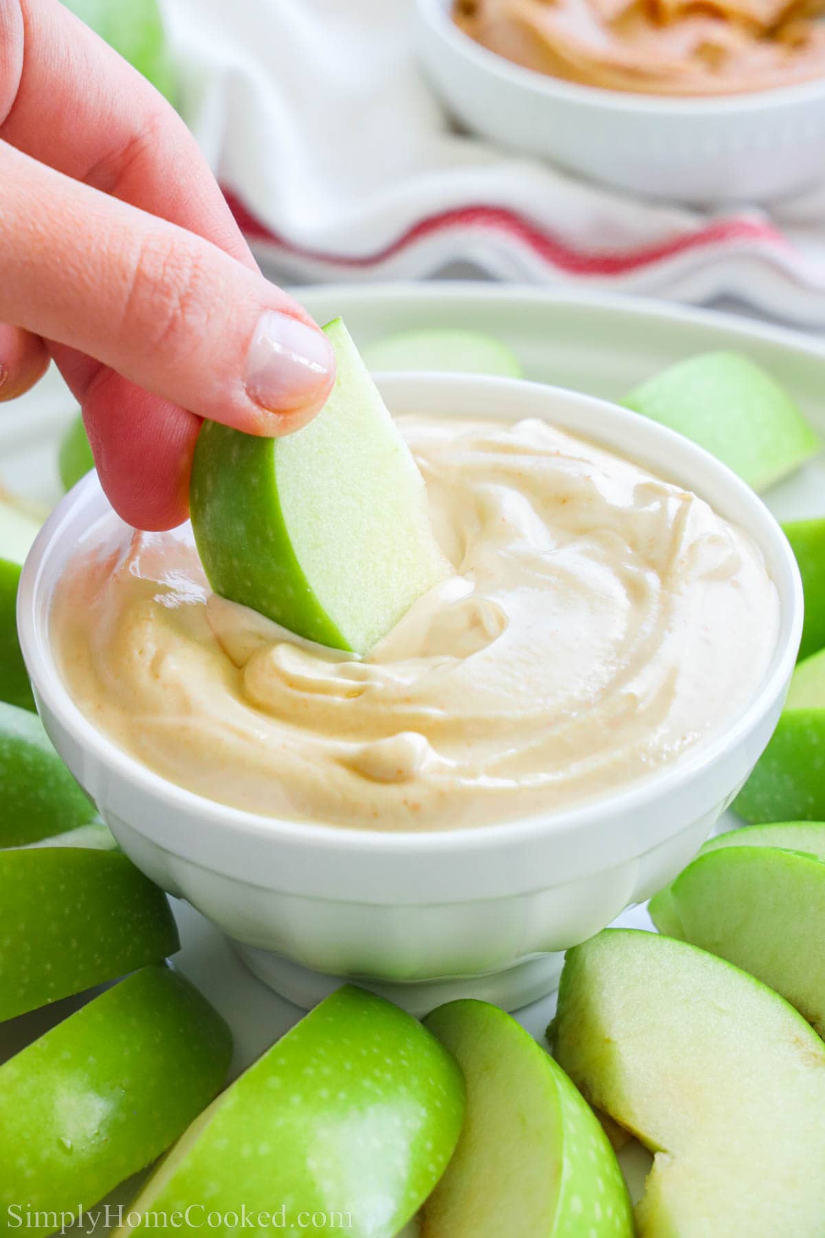 A hand dipping an apple slice into a bowl of Groundnut Butter Yogurt Dip.