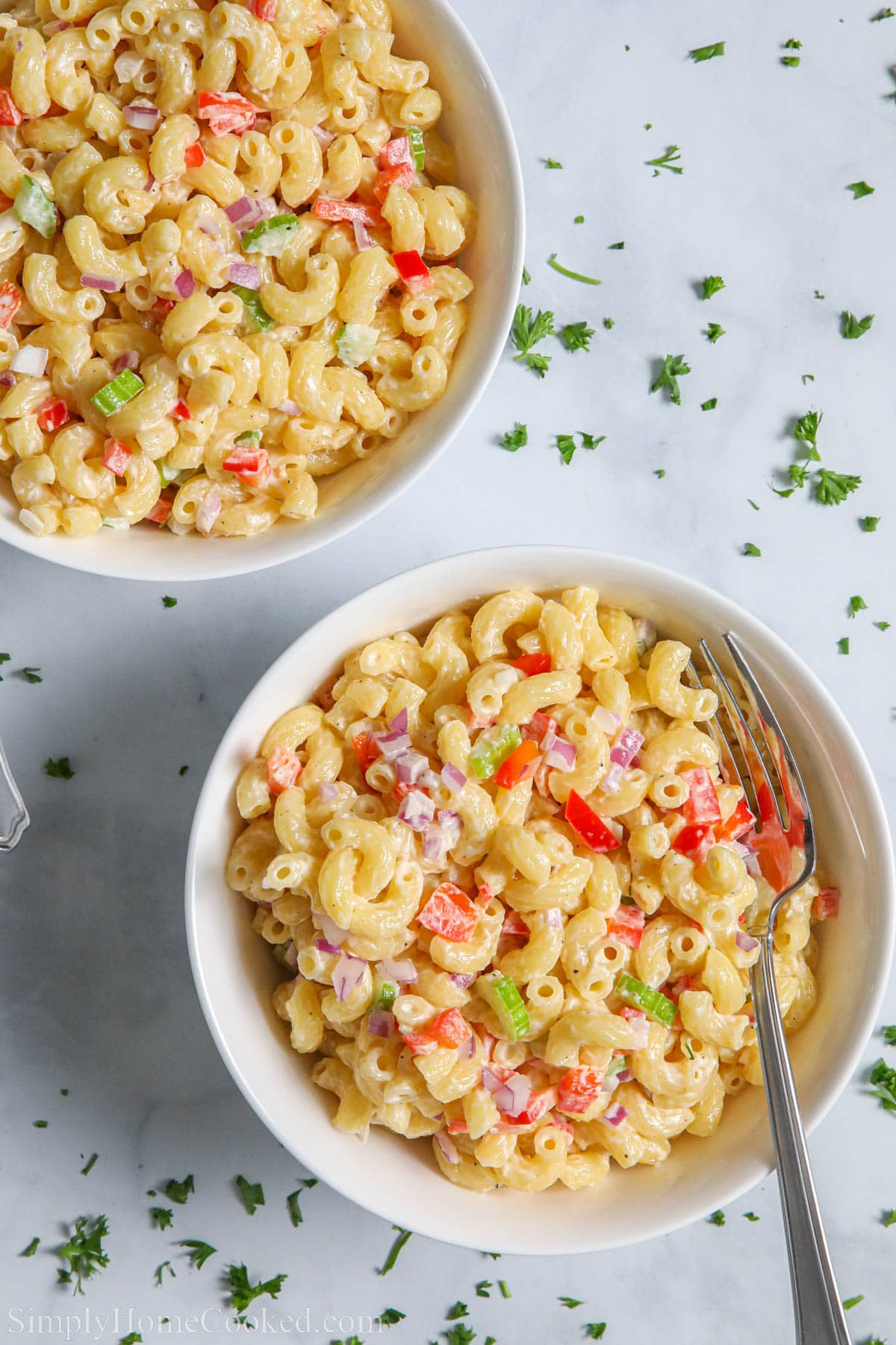 Two bowls of Luscious Pasta Salad with elbow macaroni and finely cut vegetables with forks and chopped parsley sprinkled nearby.