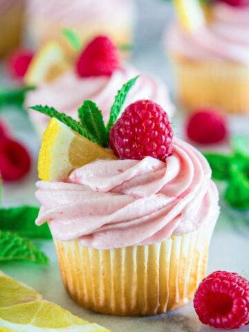 Cupcake à la framboise citronnée garni de citron, menthe et d'une framboise avec plus à proximité.