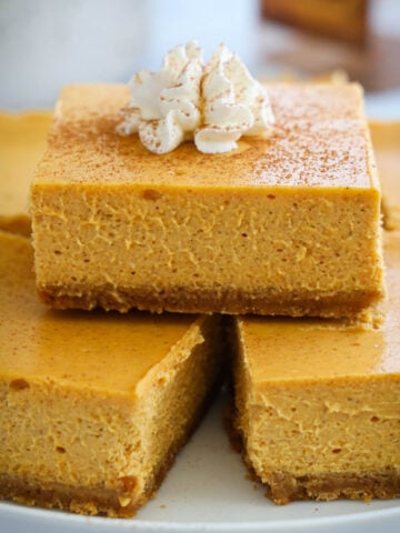 Pumpkin Cheesecke Bars stacked up and topped with whipped cream.