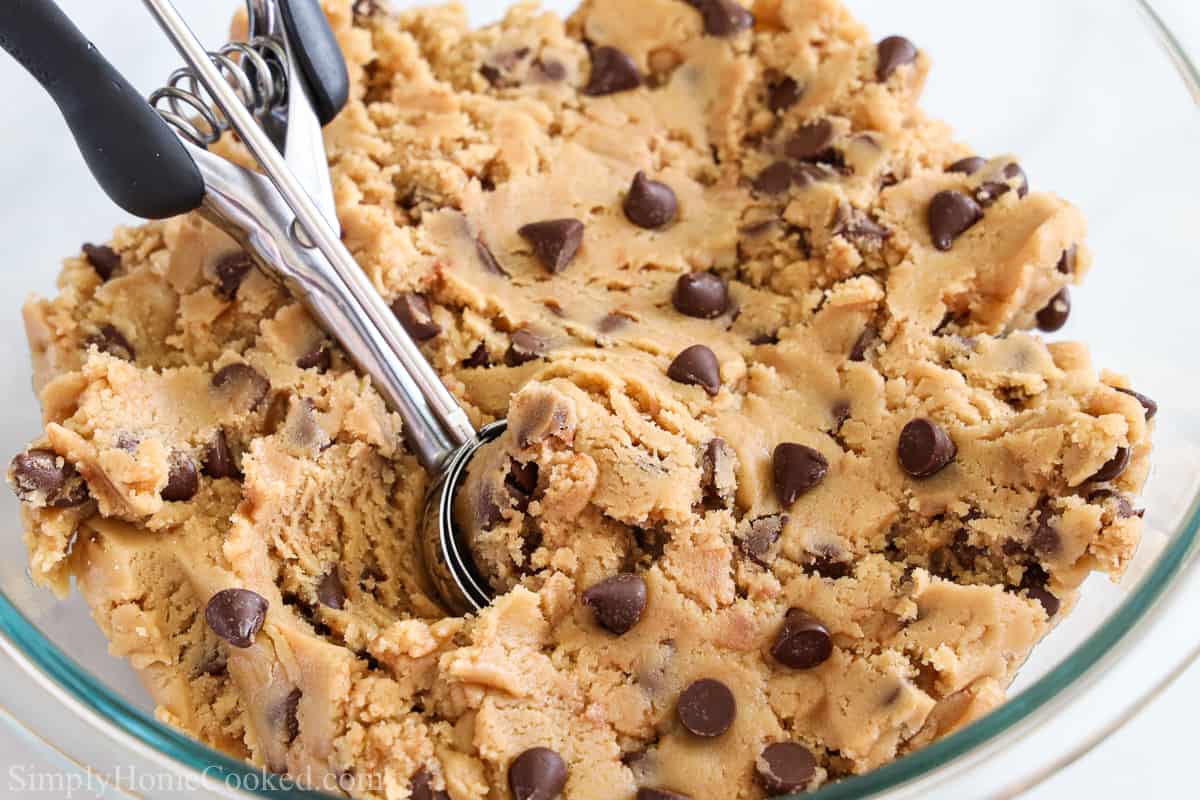 This Quick Edible Cookie Dough is fast, easy, & delicious. If you love cookie dough & want some that's safe to eat, then this one is for you. #ediblecookiedough #quickediblecookiedough #cookiedough #quickcookiedough Bowl of Quick Edible Cookie Dough with a cookie scooper in it.
