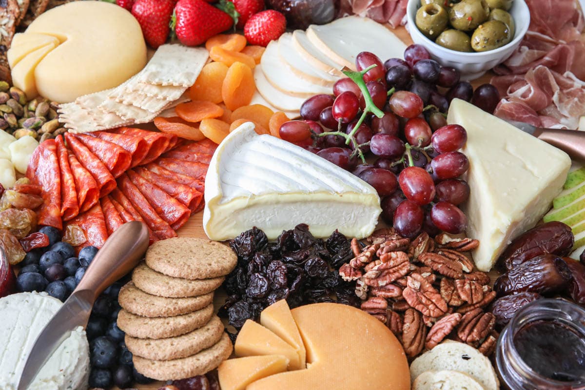 Si tu aimes la variété, alors cette Planche de Charcuterie Ultime est parfaite. Avec un mélange de fromages complémentaires, de viandes et d'autres ingrédients, tes invités vont l'adorer ! #planche-de-charcuterie-pour-fête #apéritif-de-fête #apéritif-planche-de-charcuterie #plateau-de-fromage-pour-fête Image en gros plan de l'Ultimate Charcuterie Board avec des viandes, des fromages, des noix, des fruits, des tartinades, des olives et des crackers.