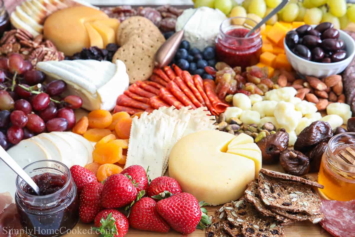 Si vous organisez une fête, vous devez savoir comment faire La Planche de Charcuterie Ultime. Ce plateau de fromage classique offre un mélange qui plaît à la foule de fruits, viandes, pains, noix, condiments et autres favoris. #charcuterie-ultime #meilleure-recette-planche-de-charcuterie-ultime #recette-de-charcuterie #comment-faire-une-planche-de-charcuterie #plateau-de-fromage Gros plan d'une Planche de Charcuterie Ultime, comprenant un assortiment de viandes, de fromages, de fruits, de noix, d'olives, de confitures, de pains, de crackers et de miel.