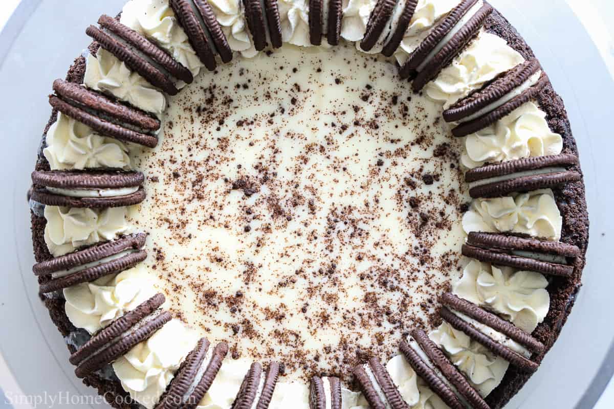 Ce Cheesecake aux Oréos est magnifique et délicieux. Vous allez adorer la crémosité délicieuse du cheesecake avec la croûte d'Oréo et le dessus de ganache. #cheesecakemaison #cheesecakeauxoréosmaison #ganachecheesecakeauxoréosmaison #recettefaciledecheesecakeauxoréos Vue aérienne d'un Cheesecake aux Oréos facile, décoré de crème fouettée, d'Oréos et de miettes de biscuits.