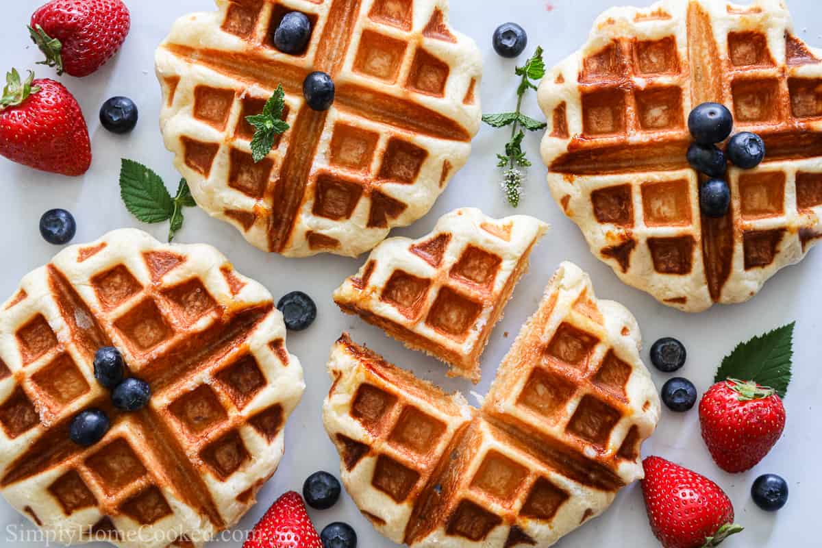 Buttery Belgian Liege Waffles sprinkled with blueberries, strawberries, and mint leaves on a white background.