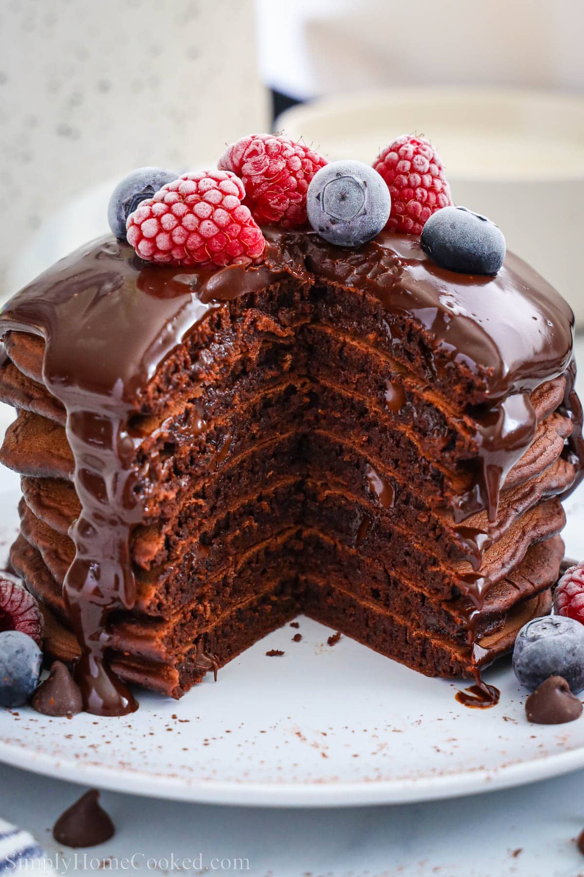 Pile de crêpes au chocolat garnies de ganache au chocolat et de baies, avec un morceau en moins.